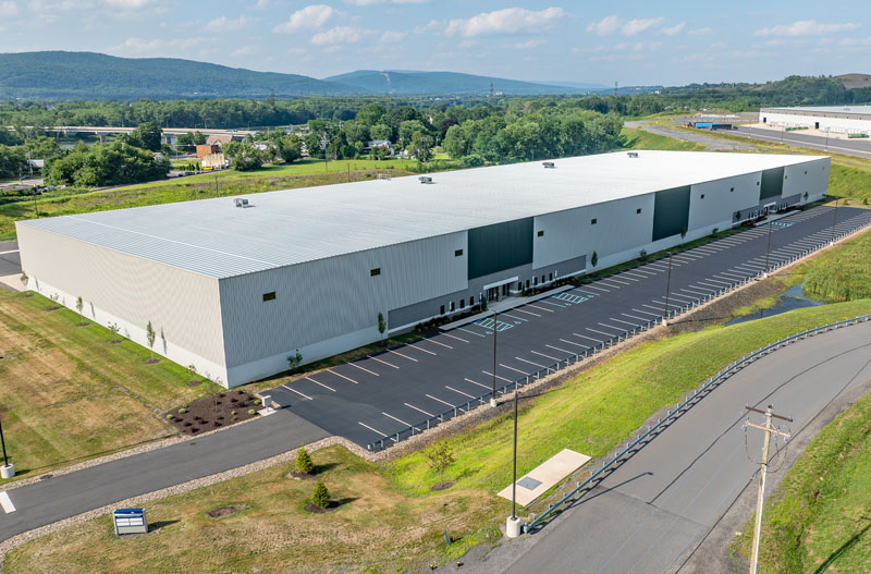 Aerial view of 144 Commonwealth Drive, a modern industrial facility with ample parking, located in the Humboldt Industrial Park in Hazle Township, PA, surrounded by scenic mountains and green landscape.